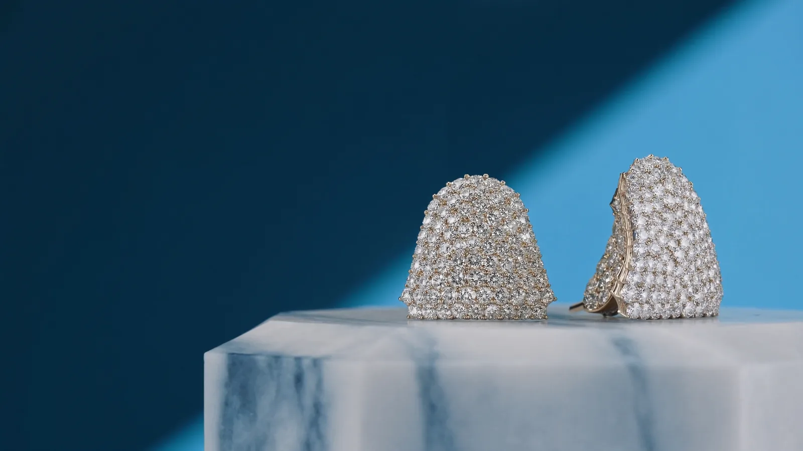 Pavé diamond earrings on a marble pedestal against the Facetz midnight and deep sky blue palette